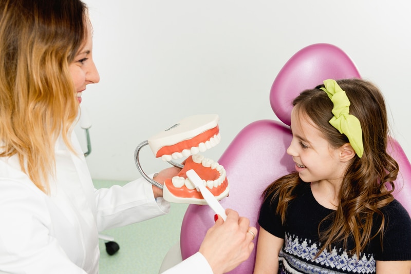 Dental hygienist showing a child how to brush her teeth