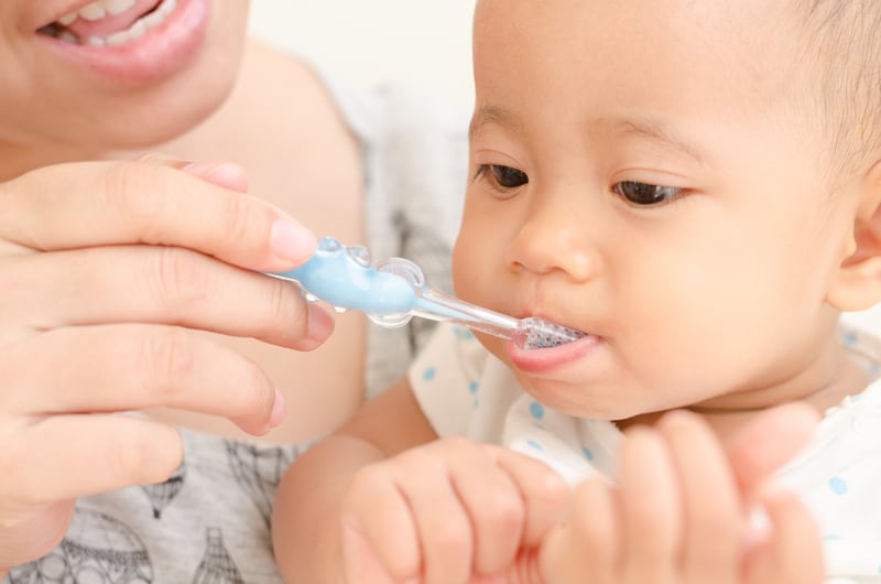 A mother brushing her small infant's baby teeth