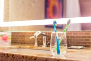 Two toothbrushes in a hotel bathroom glass cup by the sink