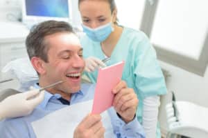Dental hygienists helping a patient to see the dental things they are explaining to him as he looks in a mirror. 