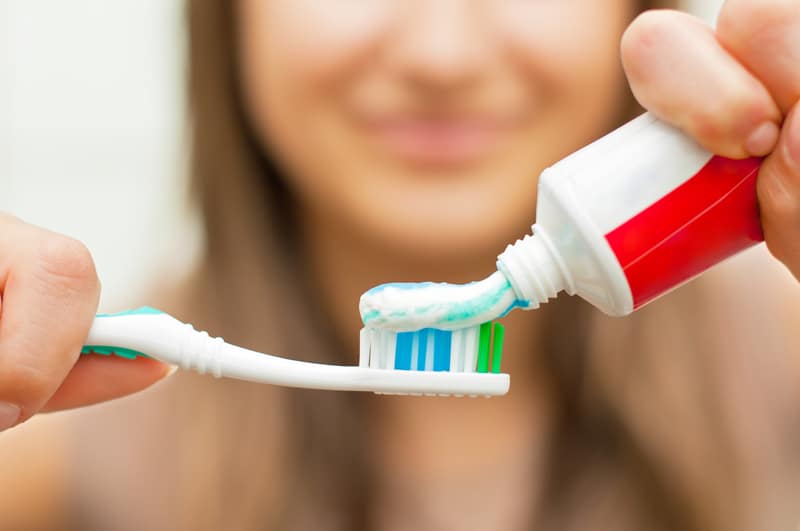 A woman putting toothpaste on a toothbrush. Everything except the woman is in focus.