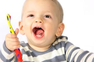 A young male child that has a few baby teeth in the mouth and he is holding a toothbrush.