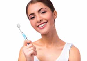 Young adult woman with ceramic braces on her teeth that is smiling and holding a toothbrush.