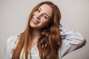 Redheaded woman that is smiling and wearing clear braces. 