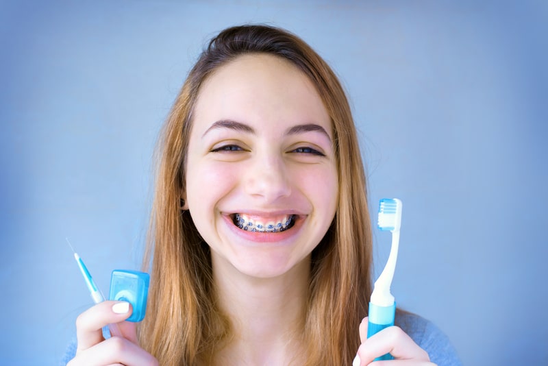 Young adult woman holding oral hygiene products like floss and toothpaste to clean her braces with.
