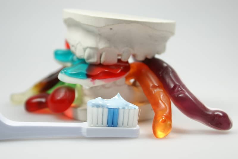 White model of the teeth that has gummy worms between the two jaws and a toothbrush lying in front of it with toothpaste on it. 