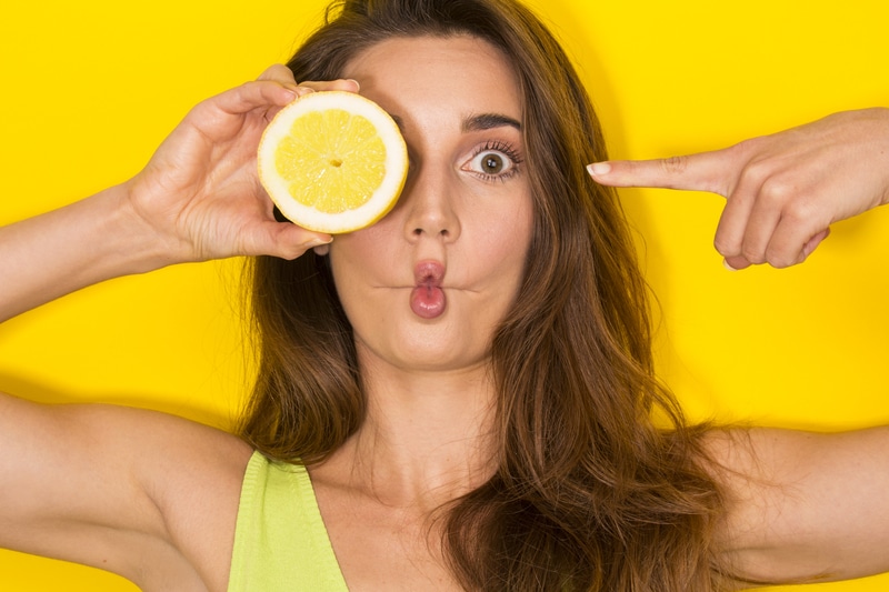 Woman making a sour face and holding up a citrus lemon section to one of her eyes.