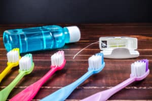 Four different colored toothbrushes, floss and a bottle of blue mouthwash on top of a wood surface.