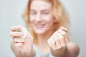 A woman that is holding floss out in front of her. The floss in her two hands is in focus, but the woman's face is blurry in the background.