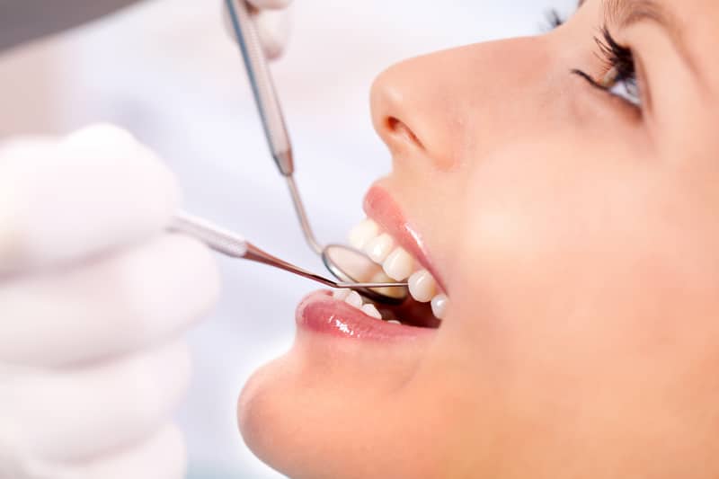 A close-up view of a woman patient that is having her teeth examined with dental tools.