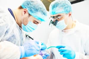 Two dental professionals wearing gloves, hair nets and face masks that are doing dental work on a patient's mouth.