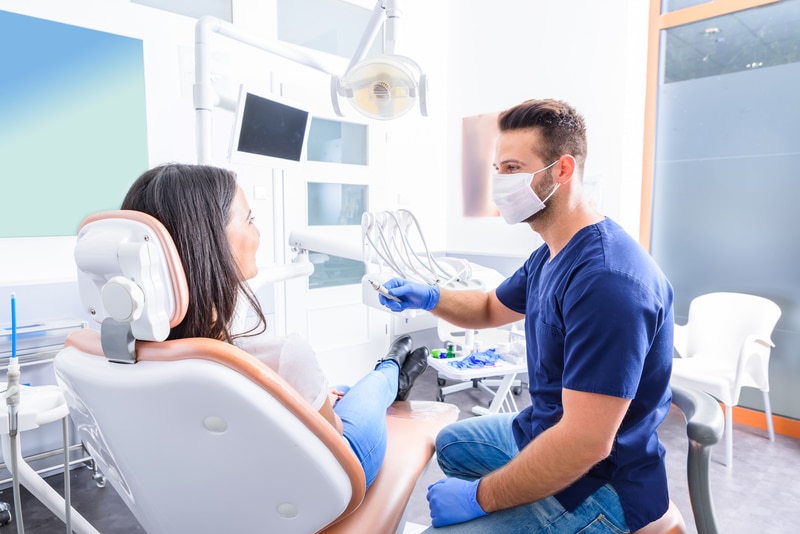 A woman patient that is speaking with a dental professional as she sits in a dental chair. 