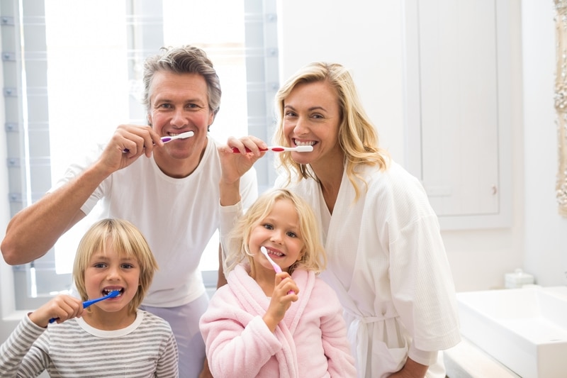 A family of four that is all brushing their teeth together in their shirts and bathrobes.
