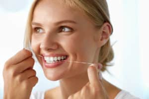 A beautiful, young adult woman that is flossing her teeth as she smiles off to the left.