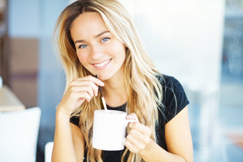 A young adult blonde woman that is about to sip on a beverage from a mug using a straw.