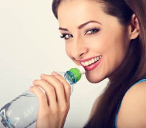 A young adult brunette woman that is about to drink a bottle of water.