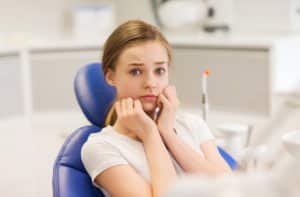 A young woman that looks really nervous to be in a dental chair.