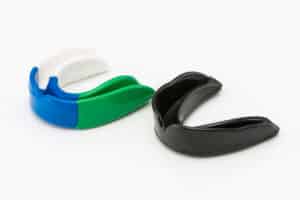 A white background that has two different mouthguards. One is black and the other is multicolored.