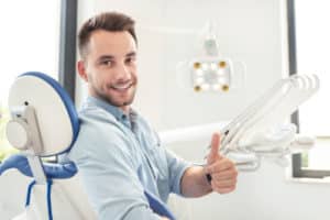 Man showing thumbs up and smiling sitting on the dental chair