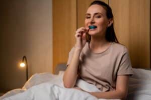 Woman in bed with oral appliance in her mouth to avoid snoring and other symptoms of obstructive sleep apnea