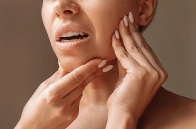 A close-up shot of a woman with TMJ holding her jaw