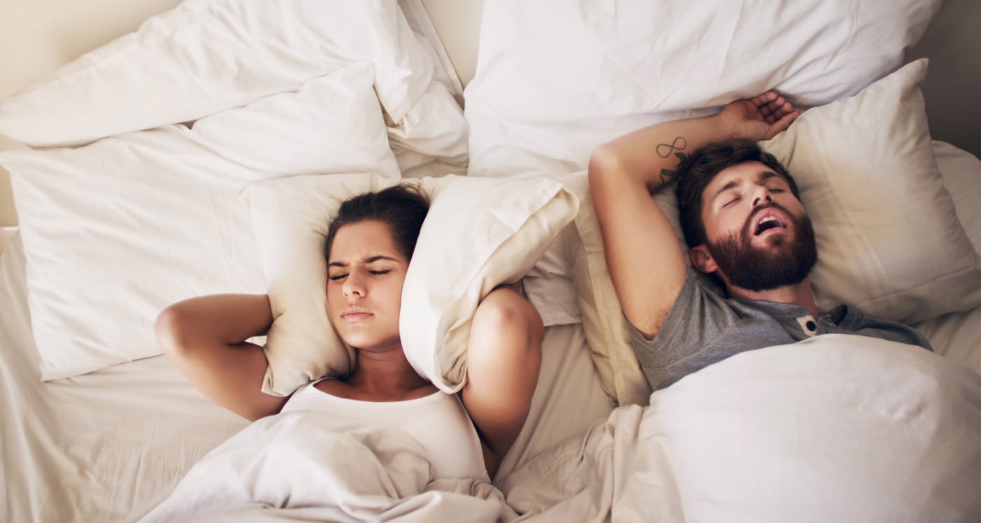 Man with sleep apnea snoring next to woman with pillow over her ears